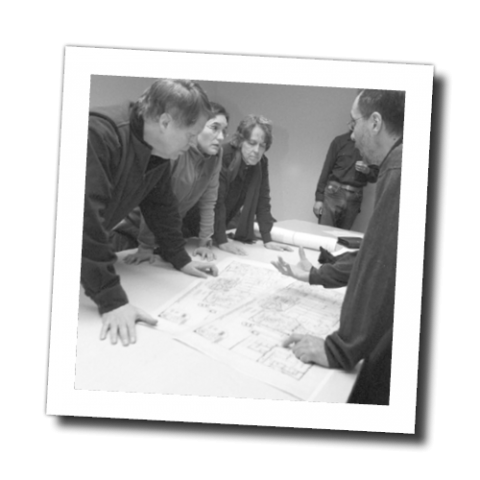 Photo of a group of people standing around a table reviewing blueprints
