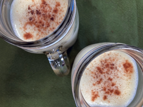 Top down view of two mugs of eggnog on a green tablecloth